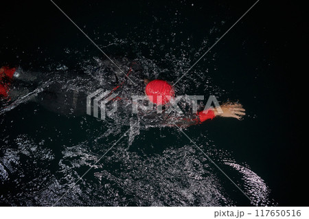 A determined professional triathlete undergoes rigorous night time training in cold waters, showcasing dedication and resilience in preparation for an upcoming triathlon swim competition 117650516