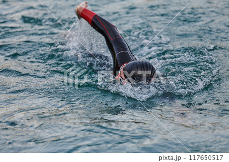 A professional triathlete trains with unwavering dedication for an upcoming competition at a lake, emanating a sense of athleticism and profound commitment to excellence. A professional triathlete trains with unwavering dedication for an upcoming competition at a lake, emanating a sense of athleticism and profound commitment to excellence. 117650517