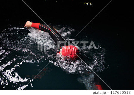 A determined professional triathlete undergoes rigorous night time training in cold waters, showcasing dedication and resilience in preparation for an upcoming triathlon swim competition 117650518