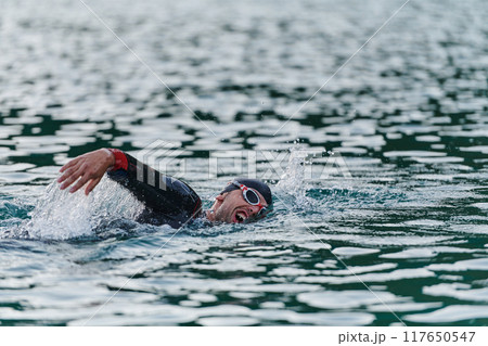 A professional triathlete trains with unwavering dedication for an upcoming competition at a lake, emanating a sense of athleticism and profound commitment to excellence. 117650547