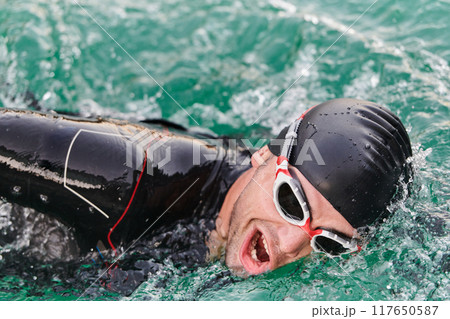 A professional triathlete trains with unwavering dedication for an upcoming competition at a lake, emanating a sense of athleticism and profound commitment to excellence. 117650587