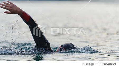 A professional triathlete trains with unwavering dedication for an upcoming competition at a lake, emanating a sense of athleticism and profound commitment to excellence. 117650634