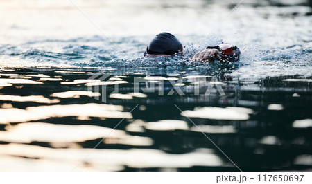 Triathlon athlete swimming on lake in sunrise wearing wetsuit 117650697
