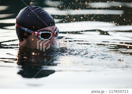 A triathlete finds serene rejuvenation in a lake, basking in the tranquility of the water after an intense training session 117650721