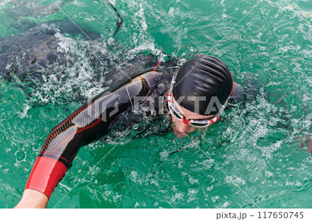 A professional triathlete trains with unwavering dedication for an upcoming competition at a lake, emanating a sense of athleticism and profound commitment to excellence. 117650745