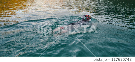 A professional triathlete trains with unwavering dedication for an upcoming competition at a lake, emanating a sense of athleticism and profound commitment to excellence. 117650748