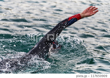 A professional triathlete trains with unwavering dedication for an upcoming competition at a lake, emanating a sense of athleticism and profound commitment to excellence. 117650909
