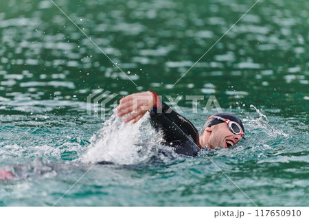 A professional triathlete trains with unwavering dedication for an upcoming competition at a lake, emanating a sense of athleticism and profound commitment to excellence. 117650910