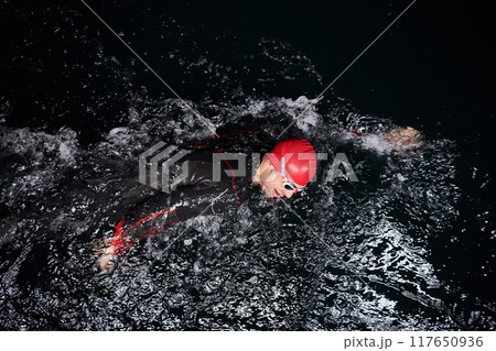 A determined professional triathlete undergoes rigorous night time training in cold waters, showcasing dedication and resilience in preparation for an upcoming triathlon swim competition 117650936