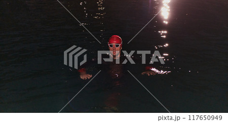 A determined professional triathlete undergoes rigorous night time training in cold waters, showcasing dedication and resilience in preparation for an upcoming triathlon swim competition 117650949