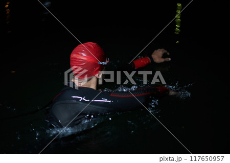 A determined professional triathlete undergoes rigorous night time training in cold waters, showcasing dedication and resilience in preparation for an upcoming triathlon swim competition A determined professional triathlete undergoes rigorous night time training in cold waters, showcasing dedication and resilience in preparation for an upcoming triathlon swim competition 117650957