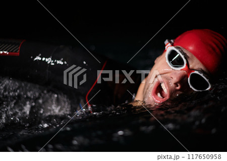 A determined professional triathlete undergoes rigorous night time training in cold waters, showcasing dedication and resilience in preparation for an upcoming triathlon swim competition 117650958