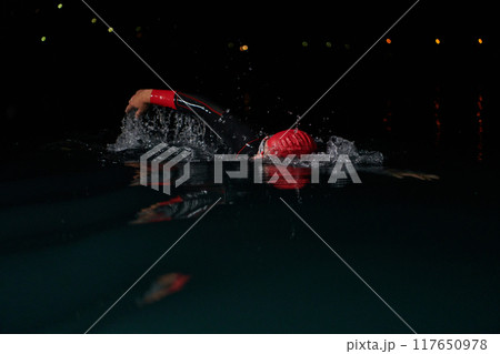 A determined professional triathlete undergoes rigorous night time training in cold waters, showcasing dedication and resilience in preparation for an upcoming triathlon swim competition 117650978
