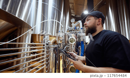Brewery technologist, focused man checking fermentation process, ensuring the highest quality standards in beer production. 117654484
