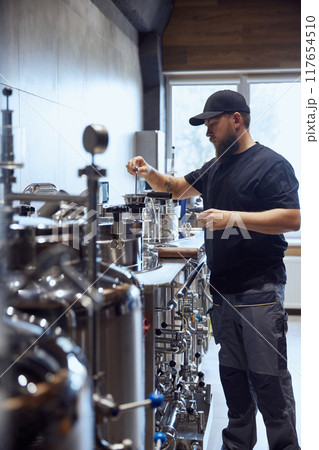 Focused on precision, brewery technologist checking brewing machinery to maintain quality in beer production process. Focused on precision, brewery technologist checking brewing machinery to maintain quality in beer production process. 117654510