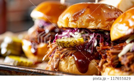 Close-up image of slow-cooked BBQ pulled pork sandwiches with coleslaw, pickles, and BBQ sauce on brioche buns, elegantly presented on a metal tray 117655829