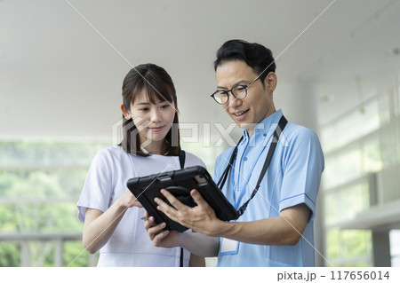 タブレットを見ながら打ち合わせをする看護師と介護士 タブレットを見ながら打ち合わせをする看護師と介護士 117656014