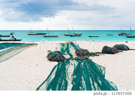 large fishing nets lying on african beach with boats near the shore large fishing nets lying on african beach with boats near the shore 117657308