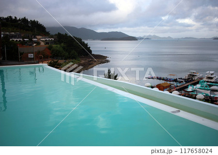 Dolsan-eup, Yeosu-si, South Korea - July 26, 2024: Young woman watching sunrise at a resort with a swimming pool overlooking the sea in Yeosu 117658024