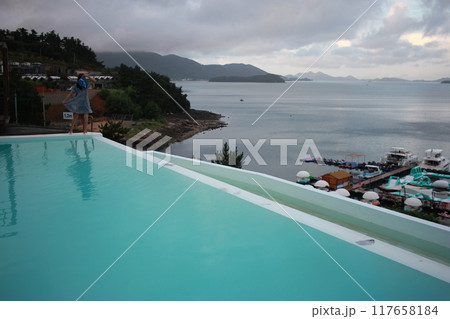 Dolsan-eup, Yeosu-si, South Korea - July 26, 2024: Young woman watching sunrise at a resort with a swimming pool overlooking the sea in Yeosu 117658184