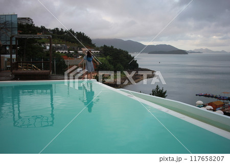 Dolsan-eup, Yeosu-si, South Korea - July 26, 2024: Young woman watching sunrise at a resort with a swimming pool overlooking the sea in Yeosu 117658207