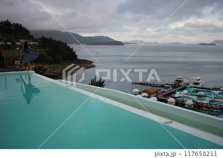 Dolsan-eup, Yeosu-si, South Korea - July 26, 2024: Young woman watching sunrise at a resort with a swimming pool overlooking the sea in Yeosu 117658211