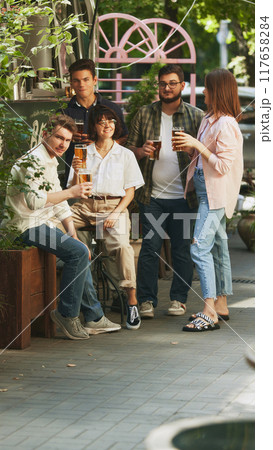 Relaxed and happy young people, men and women, friends gathering at cozy outdoor bar, pub, enjoying regressing beer. Festive atmosphere Relaxed and happy young people, men and women, friends gathering at cozy outdoor bar, pub, enjoying regressing beer. Festive atmosphere 117658284