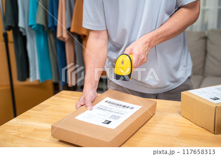 close up hands of an online seller scanning product barcoad on his product box 117658313