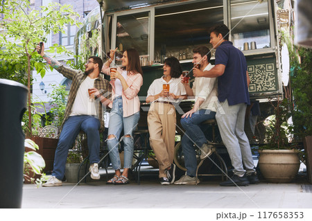 Happy smiling people, friends, men and women meeting at local outdoor bar, drinking beer and taking selfie with mobile phone. Cozy memories 117658353