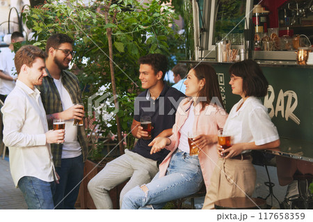 Friends gathering outdoors, meeting by trendy bar, enjoying relaxed afternoon in good company, drinking beer and having good relaxing time. Friends gathering outdoors, meeting by trendy bar, enjoying relaxed afternoon in good company, drinking beer and having good relaxing time. 117658359