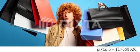 Banner. Man with colorful packages against blue studio background with negative space to insert text. Promotion code. Concept of Black Friday sale. Banner. Man with colorful packages against blue studio background with negative space to insert text. Promotion code. Concept of Black Friday sale. 117659020