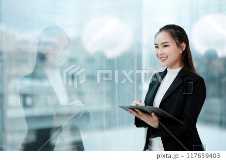 A woman in a business suit is smiling and holding a tablet A woman in a business suit is smiling and holding a tablet 117659403