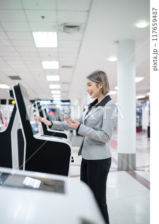 A woman is standing in front of a machine and looking at her phone A woman is standing in front of a machine and looking at her phone 117659487