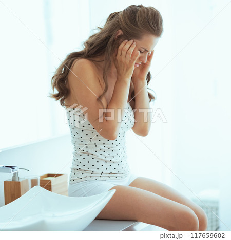 Stressed young woman sitting in bathroom 117659602