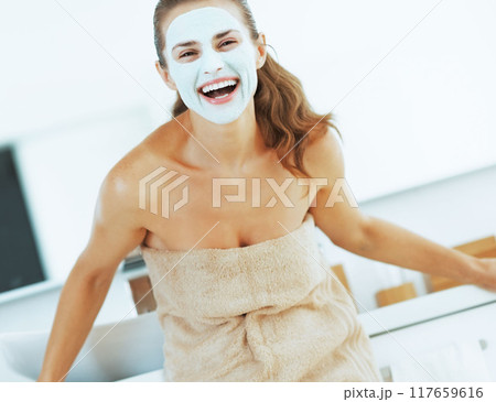 smiling young woman with facial mask in bathroom 117659616