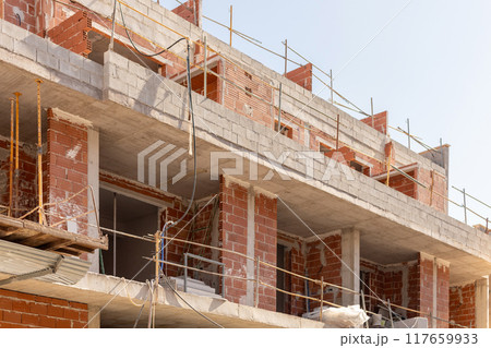 Close-up of an urban construction site with unfinished brick and concrete building under clear skies. Perfect for content related to urban development, architecture, and construction. 117659933