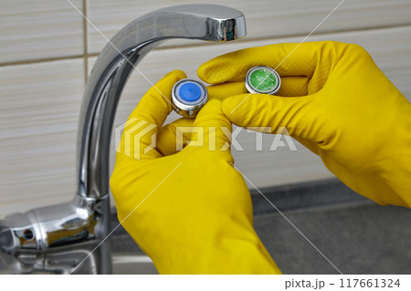 Replacing a clogged kitchen sink faucet aerator. Hands in yellow rubber gloves showing the replaced aerator 117661324