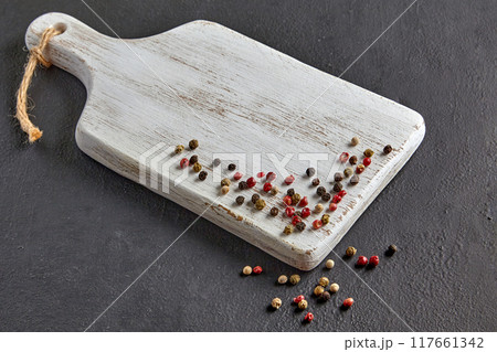 White wooden cutting board with scattered colorful peppercorns on a black stone table White wooden cutting board with scattered colorful peppercorns on a black stone table 117661342
