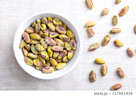 Pistachios kernels, roasted and salted nuts in a white bowl on linen fabric. Shelled fruits of Pistacia vera, crunchy toasted and salted. Ready-to-eat snack food. Close-up, from above, food photo. Pistachios kernels, roasted and salted nuts in a white bowl on linen fabric. Shelled fruits of Pistacia vera, crunchy toasted and salted. Ready-to-eat snack food. Close-up, from above, food photo. 117661938