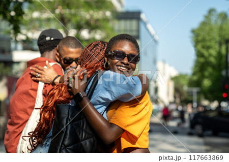 Joyful black students in good mood hugging each other in friendly warmly way on street outside. Joyful black students in good mood hugging each other in friendly warmly way on street outside. 117663869