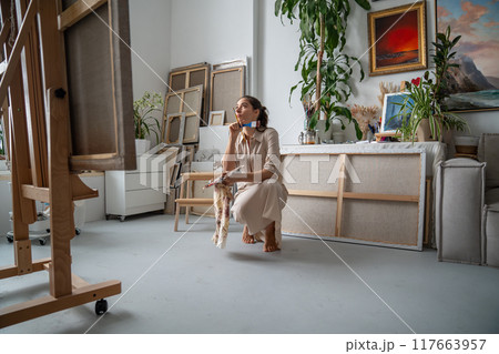 Pensive unsmiling woman artist looking up at huge canvas fixed on easel, thinking, reflecting. 117663957