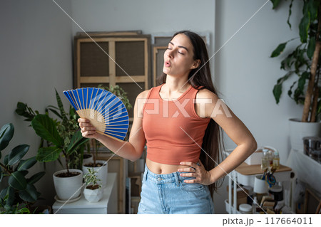 Tired unhappy overheated woman fanning herself suffering from summer heat, uncomfortable sensations 117664011