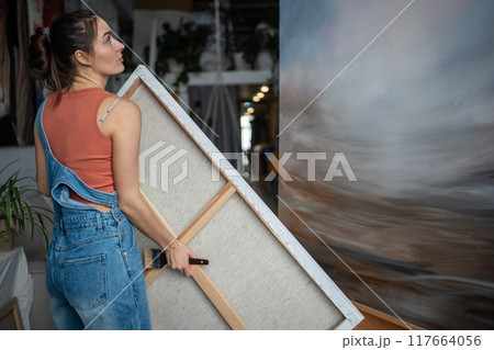 Calm thoughtful woman artist holding carrying canvas, evaluating own painting with interest. Calm thoughtful woman artist holding carrying canvas, evaluating own painting with interest. 117664056