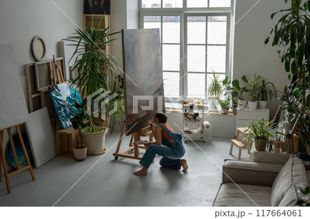 Focused concentrated woman painter working in ordered, light home art studio with lot of plants. Focused concentrated woman painter working in ordered, light home art studio with lot of plants. 117664061