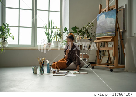 Concentrated artistic woman practicing at drawing, developing painting skills relaxing on floor. Concentrated artistic woman practicing at drawing, developing painting skills relaxing on floor. 117664107