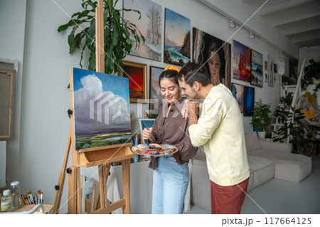 Smiling painters spouses works on painting. Happy woman artist with husband at home studio workshop Smiling painters spouses works on painting. Happy woman artist with husband at home studio workshop 117664125