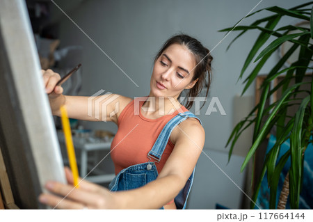 Confident proud female artist painting picture in light art studio workshop. Creative process. Confident proud female artist painting picture in light art studio workshop. Creative process. 117664144