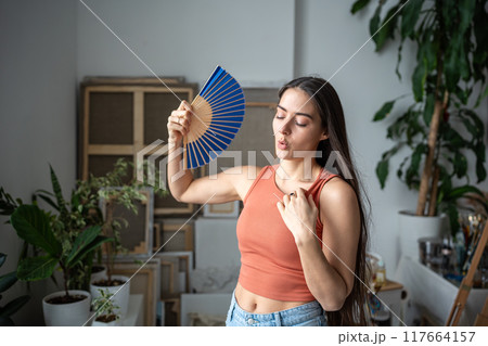 Tired unhappy overheated woman fanning herself suffering from summer heat, uncomfortable sensations Tired unhappy overheated woman fanning herself suffering from summer heat, uncomfortable sensations 117664157