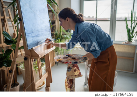 Serious female artist working on artwork masterpiece, deeply immersed in creative art process. 117664159