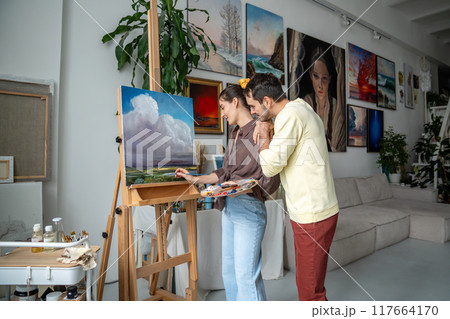 Creative woman artist paints picture in art studio, loving man husband supportive and enjoys process 117664170